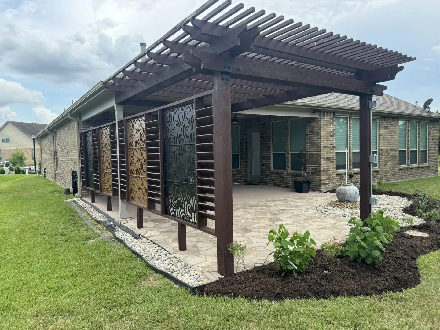 Backyard outdoor living retreat with cedar pergola, custom privacy panels, stone patio, water feature, and landscape beds in The Woodlands, Texas.