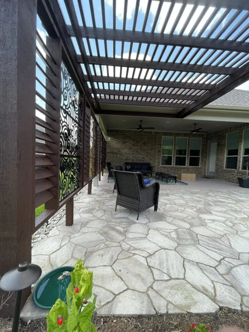 Stone patio with cedar pergola, custom privacy panels, wicker seating, and landscaped garden bed in The Woodlands, Texas.