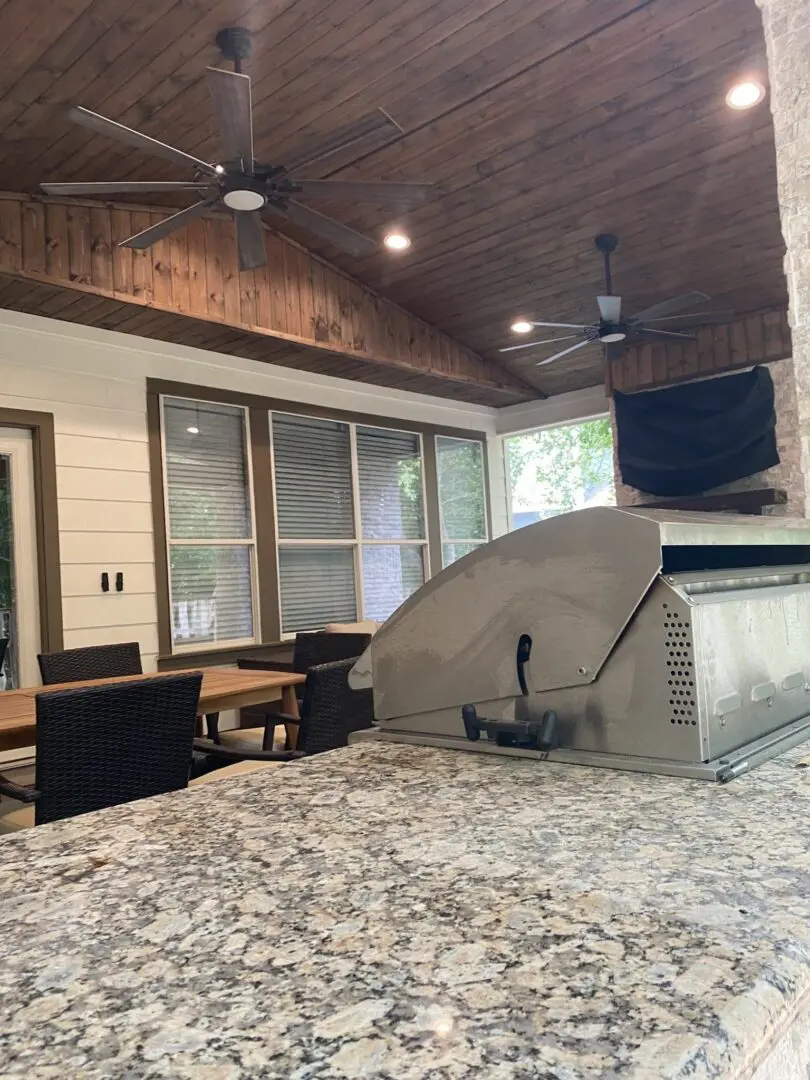 Outdoor kitchen countertop with granite finish, ceiling fans, and dining area under wood ceiling patio cover in The Woodlands.