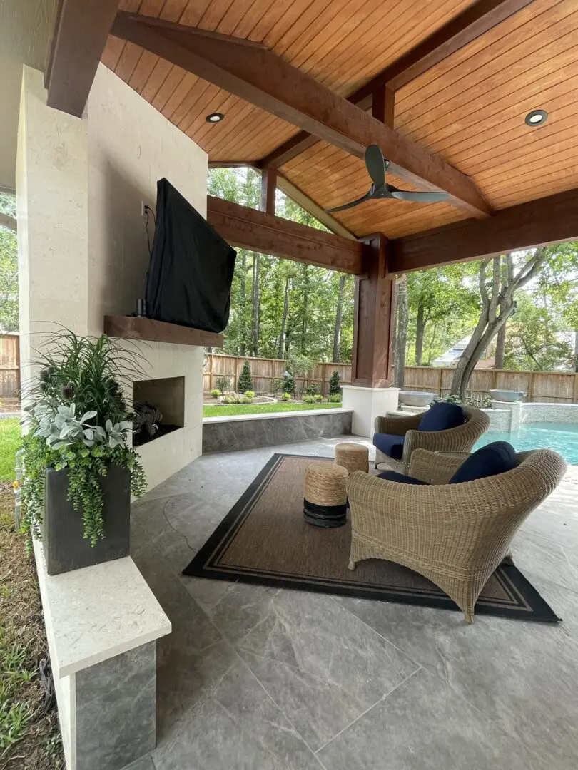 Covered patio with stone fireplace, lounge seating, and poolside view in The Woodlands TX