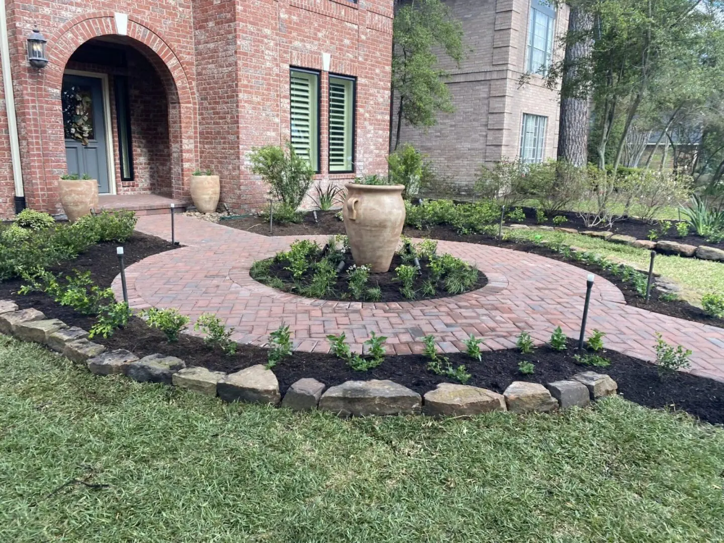 Front yard brick walkway with circular urn centerpiece and landscaped garden by JM Outdoor Living in The Woodlands, Texas.