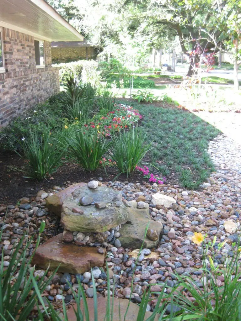 Front yard landscaping with stone fountain, dry creek riverbed, and colorful flowers in The Woodlands TX by JM Outdoor Living.