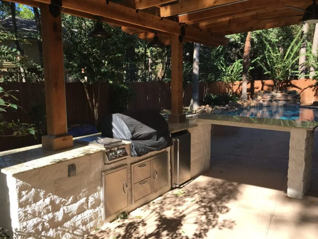 Outdoor kitchen with pergola roof, granite countertop, and stainless steel grill in The Woodlands