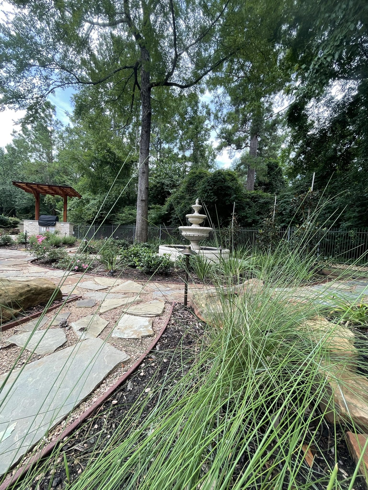 Serene garden path with stone tiles and tall grasses near a water fountain.