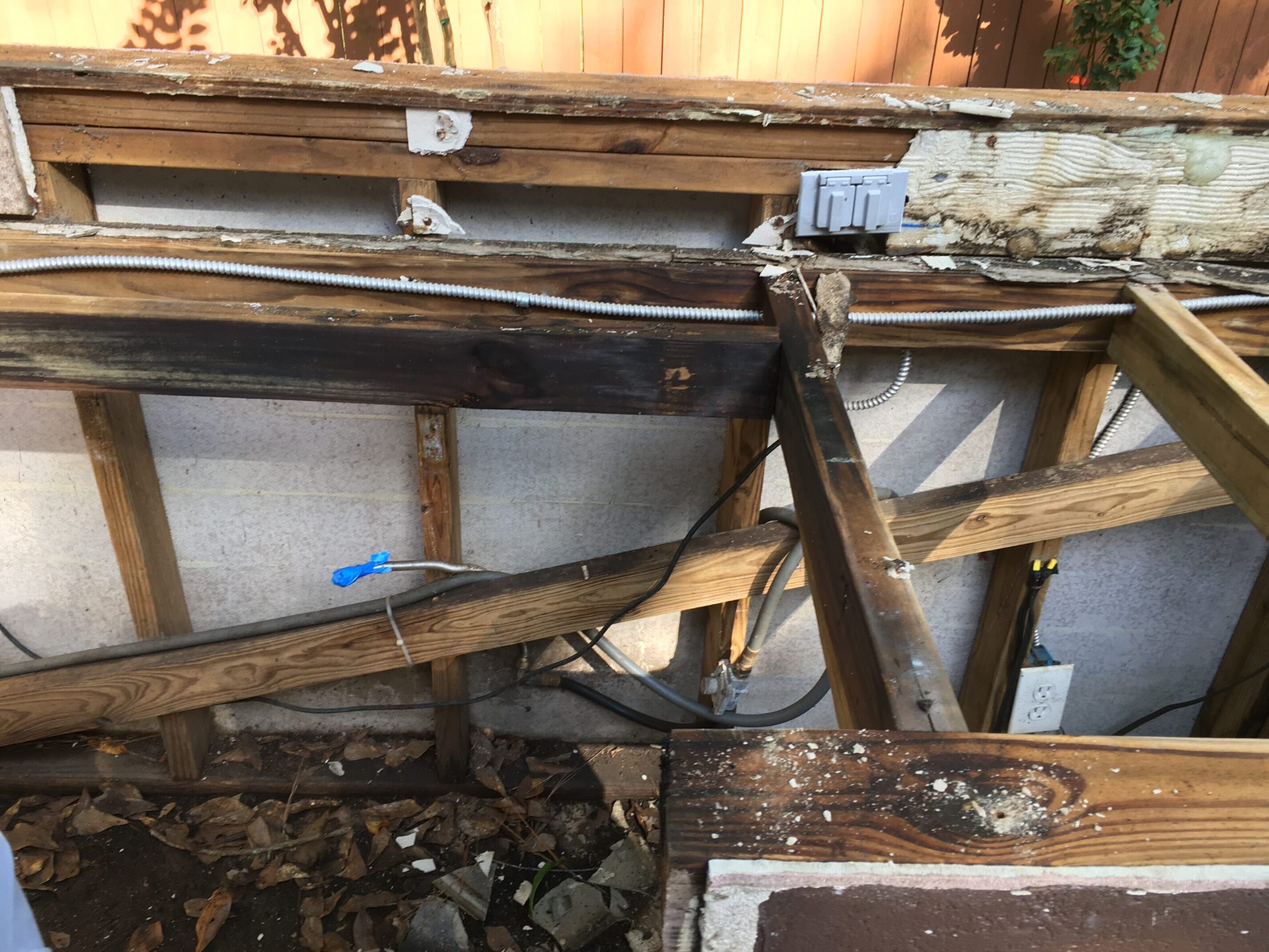 Before photo showing damaged outdoor kitchen framing with exposed wiring and rotted wood after fire damage in The Woodlands, Texas.