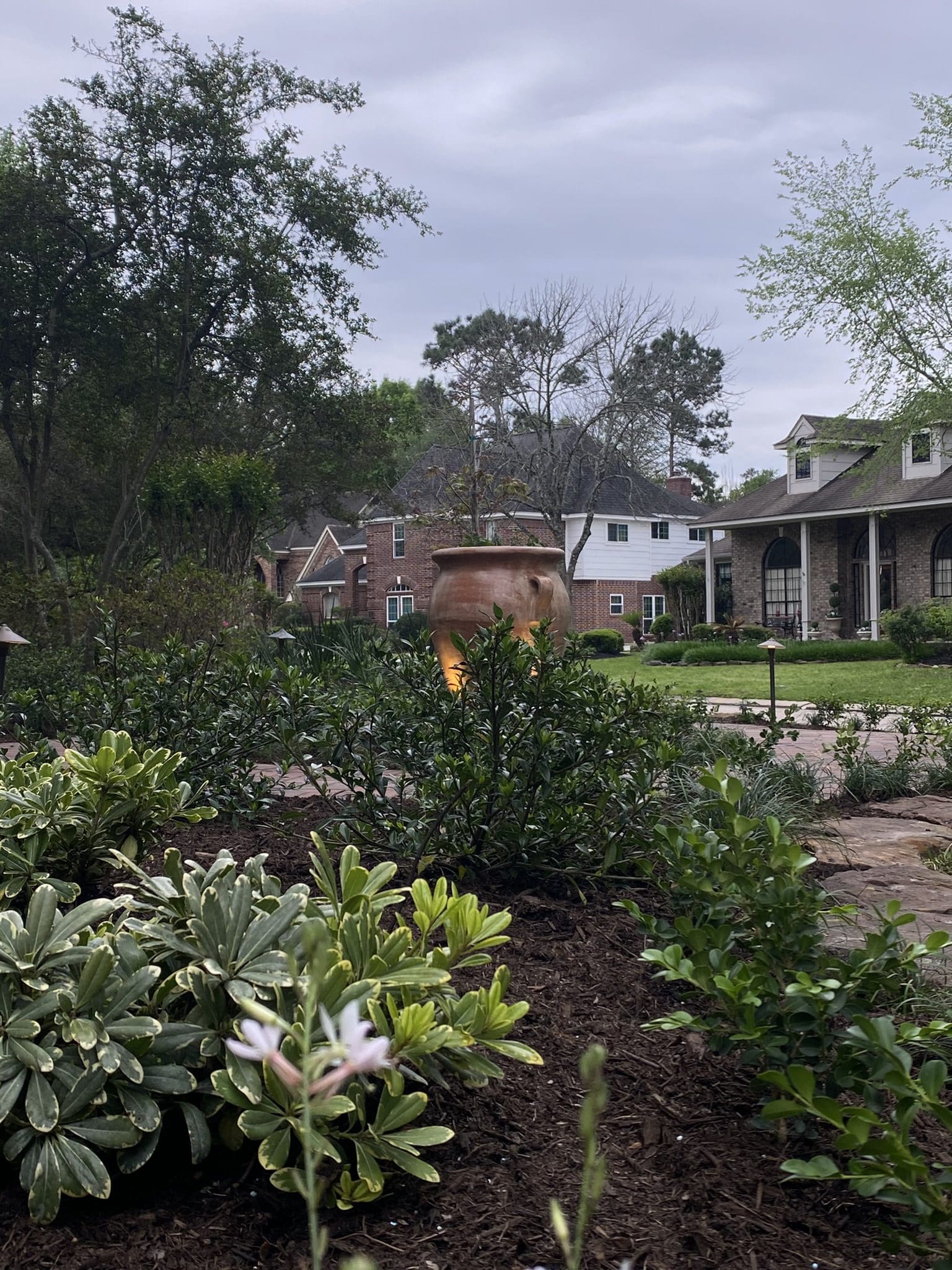 Layered front yard landscape with fresh shrubs, mulched beds, and illuminated urn centerpiece in a custom design in The Woodlands, Texas.