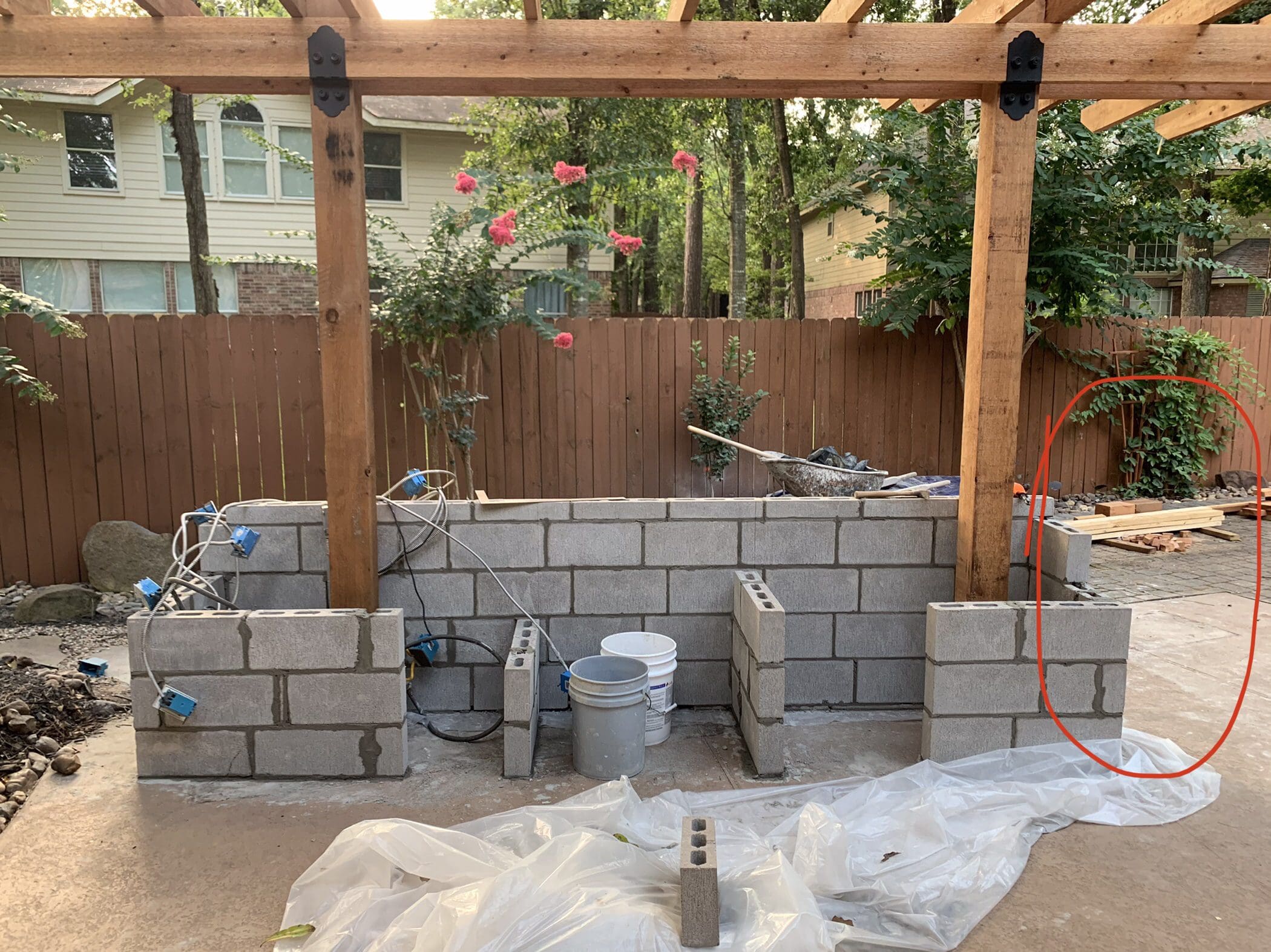 Progress photo showing masonry block outdoor kitchen construction with electrical outlets under a cedar pergola in The Woodlands, Texas.