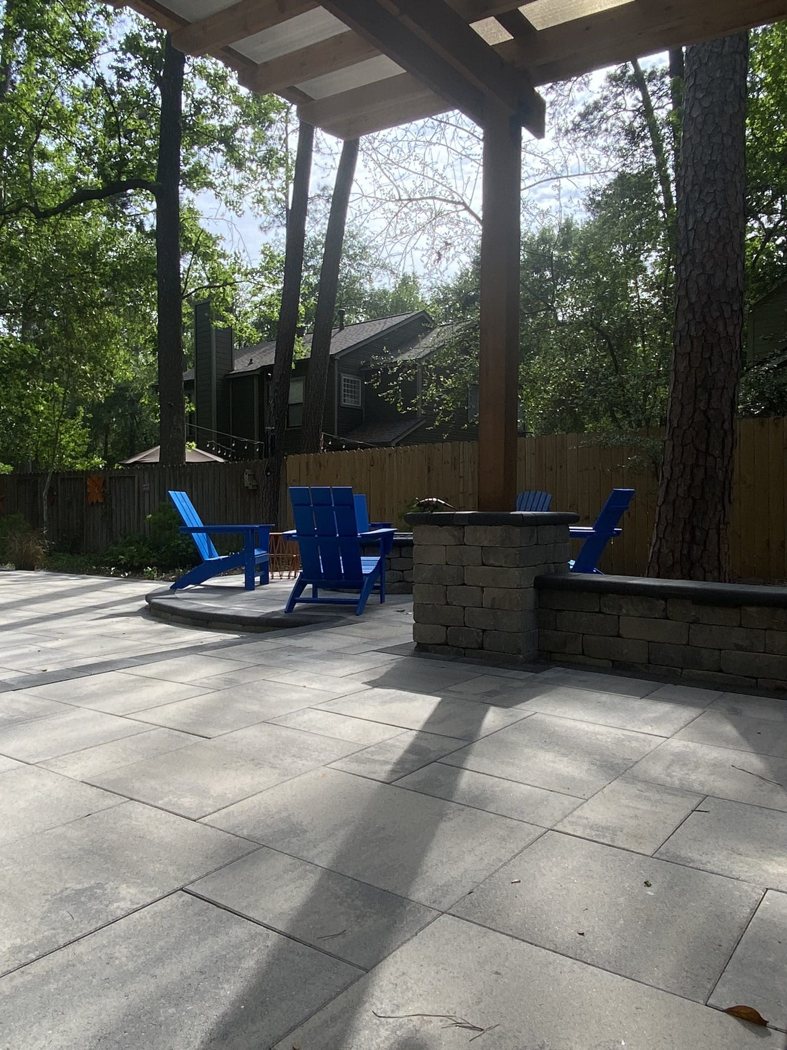Outdoor patio with blue chairs and stone seating area surrounded by trees.