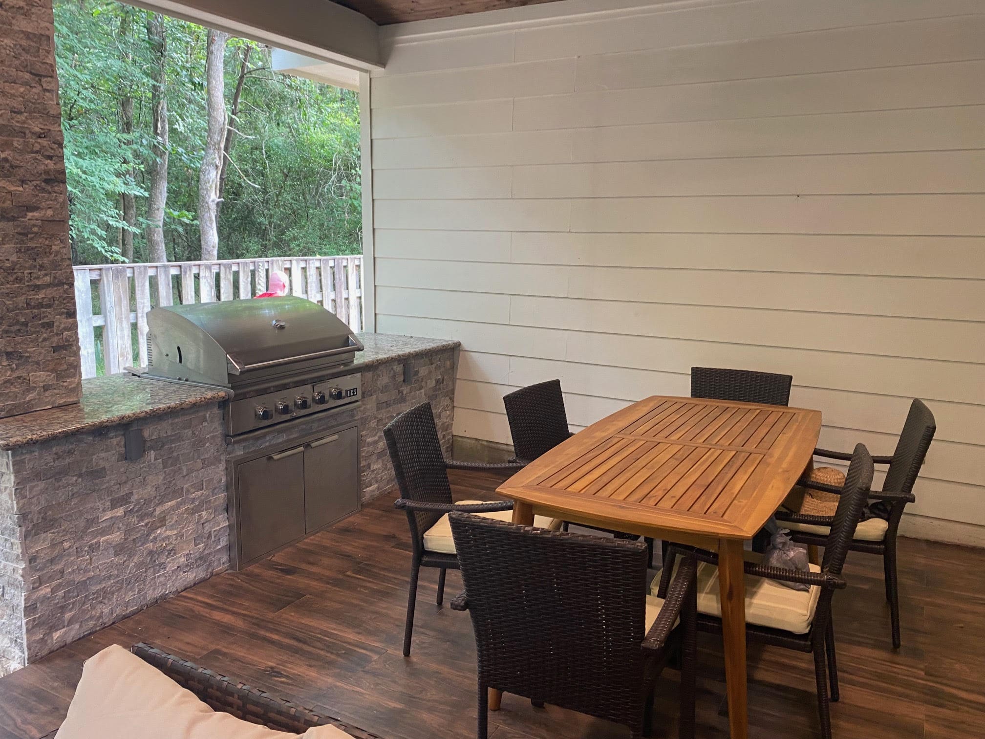 Outdoor kitchen in The Woodlands featuring built-in grill, granite countertop, and patio dining area under a covered space.