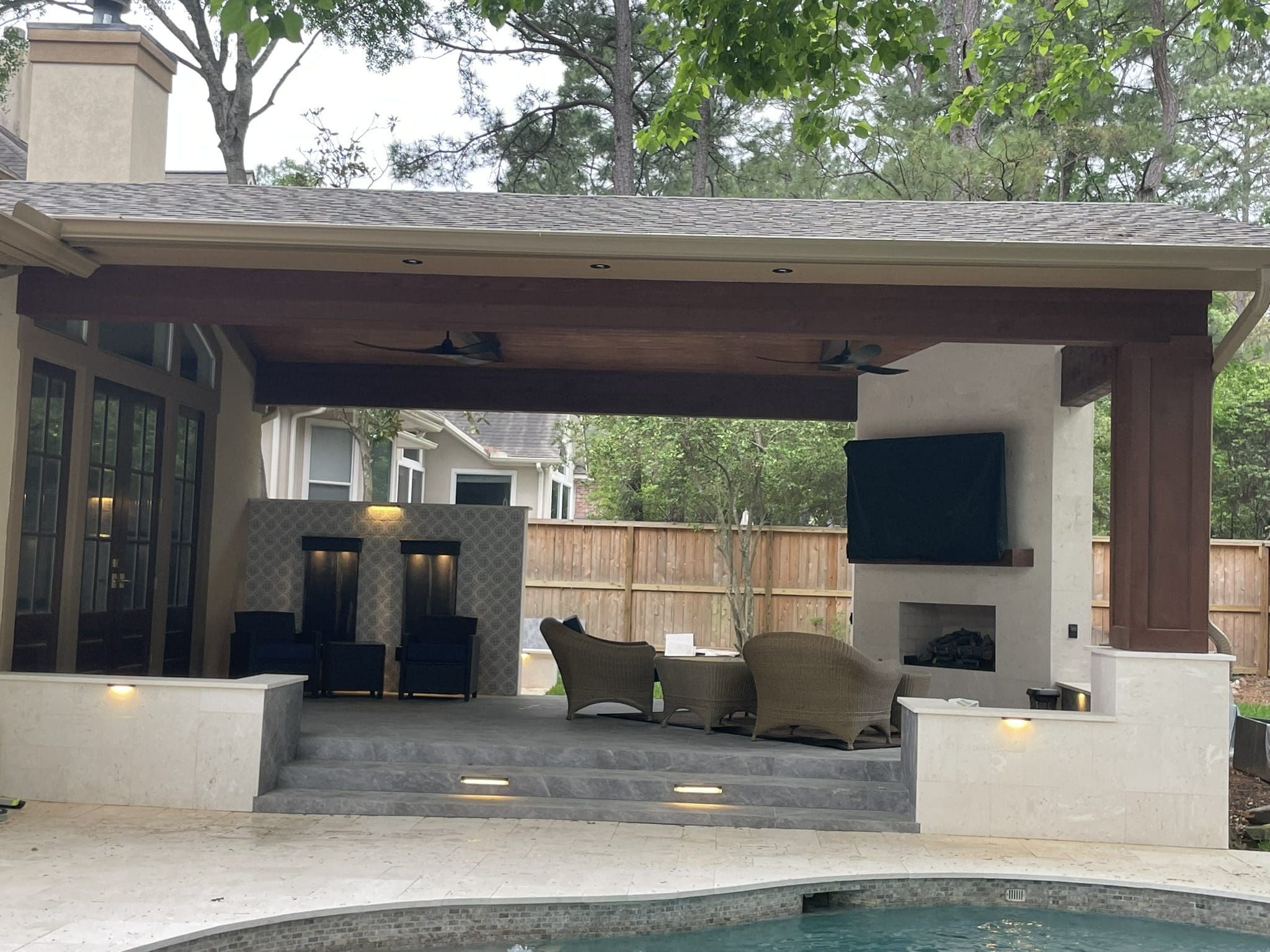 Luxury patio cover in The Woodlands, TX with outdoor fireplace, modern water wall, and lounge seating designed by JM Outdoor Living.
