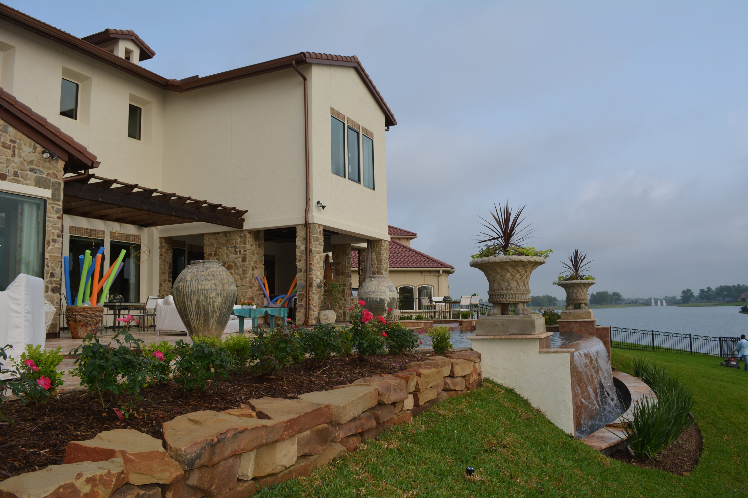 Backyard outdoor living space with pergola, urn fountain, and landscaped beds at AISD Showcase Home in The Woodlands by JM Outdoor Living