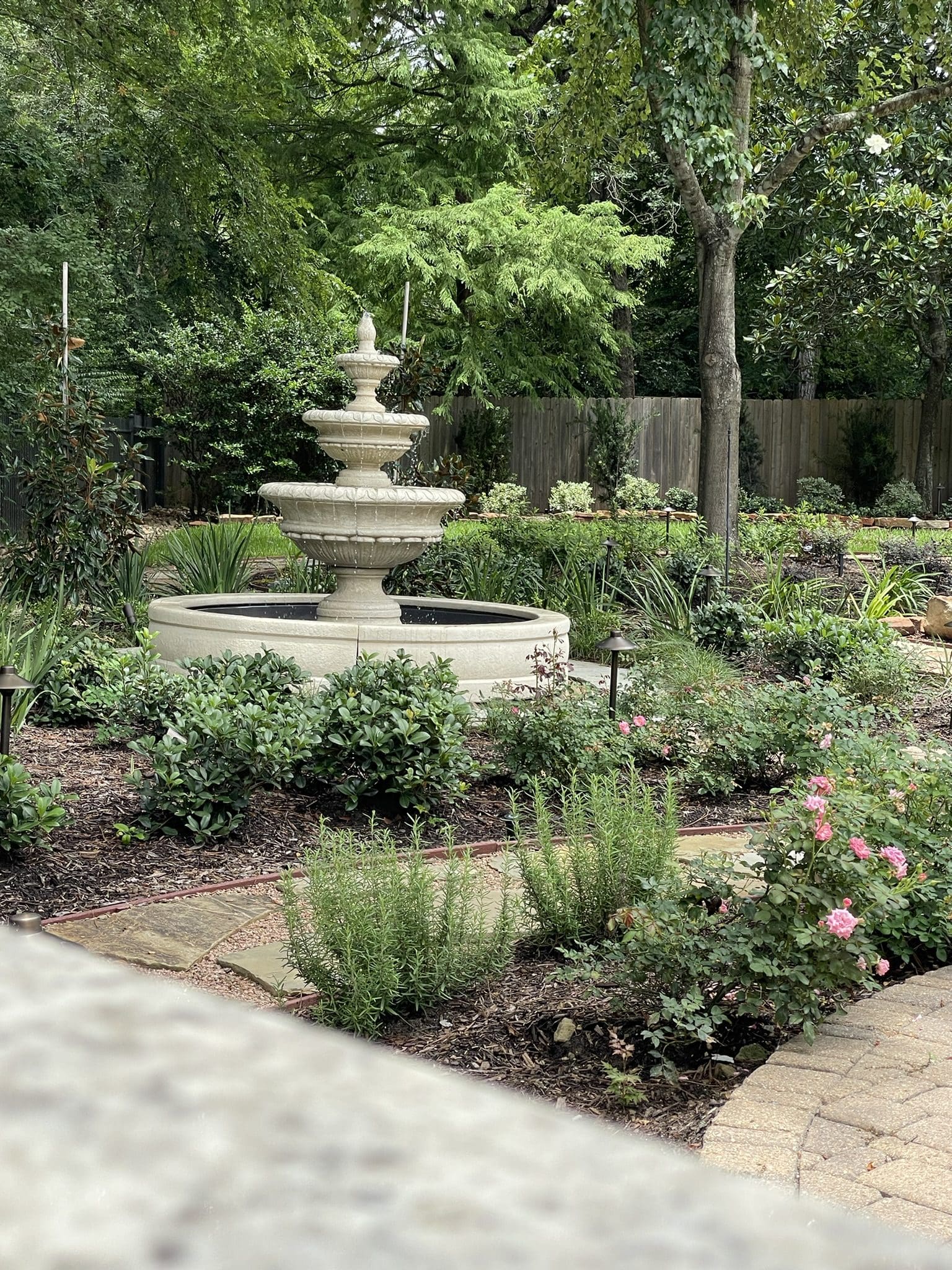 Elegant stone fountain surrounded by lush garden plants and trees.